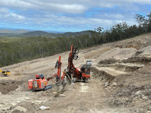 Two drill rigs next to a slope with sections undergoing drill and blasting" by Beards team.